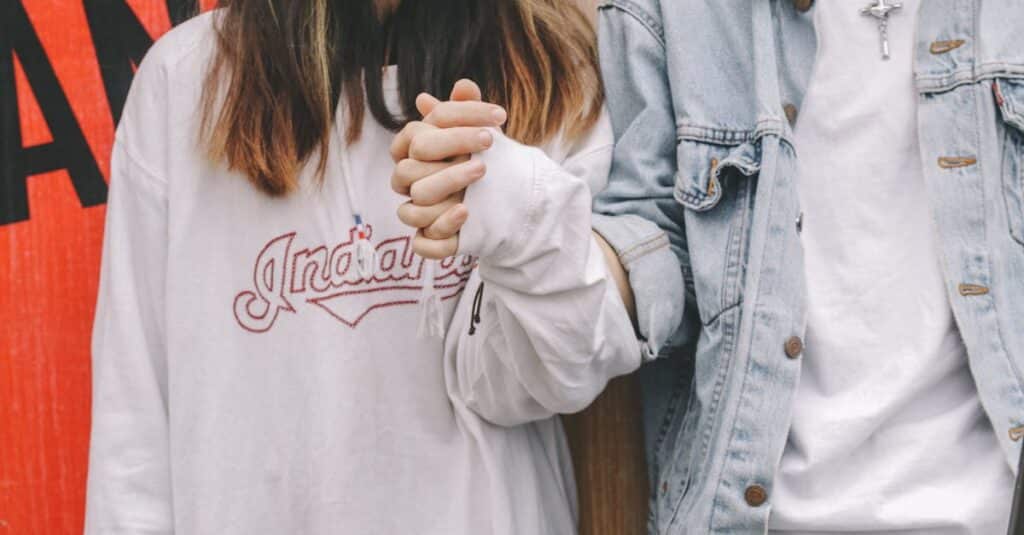 Young couple holding hands in casual attire, symbolizing love and togetherness.